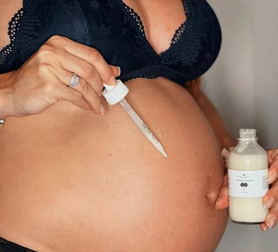 Applying True Belly Serum with the dropper to a pregnant belly